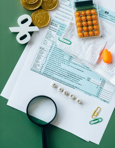 Top view of tax forms, calculator, coins, and office supplies on a green desk.
